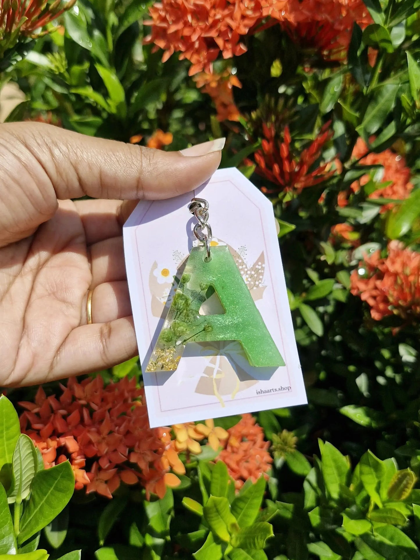 Hand holding a card with a green dress design in front of orange flowers